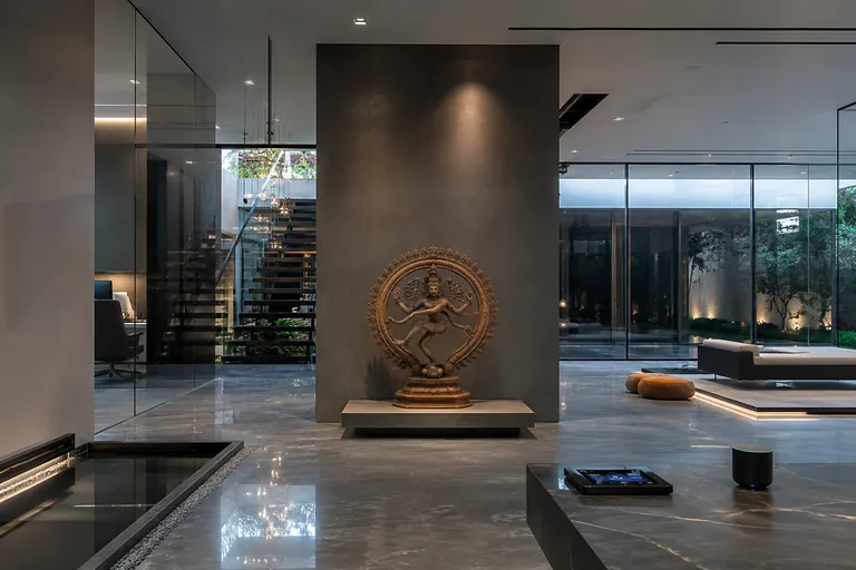IVARA stone deity sculpture displayed on a dark timber cabinet in a warm-toned plaster corridor.